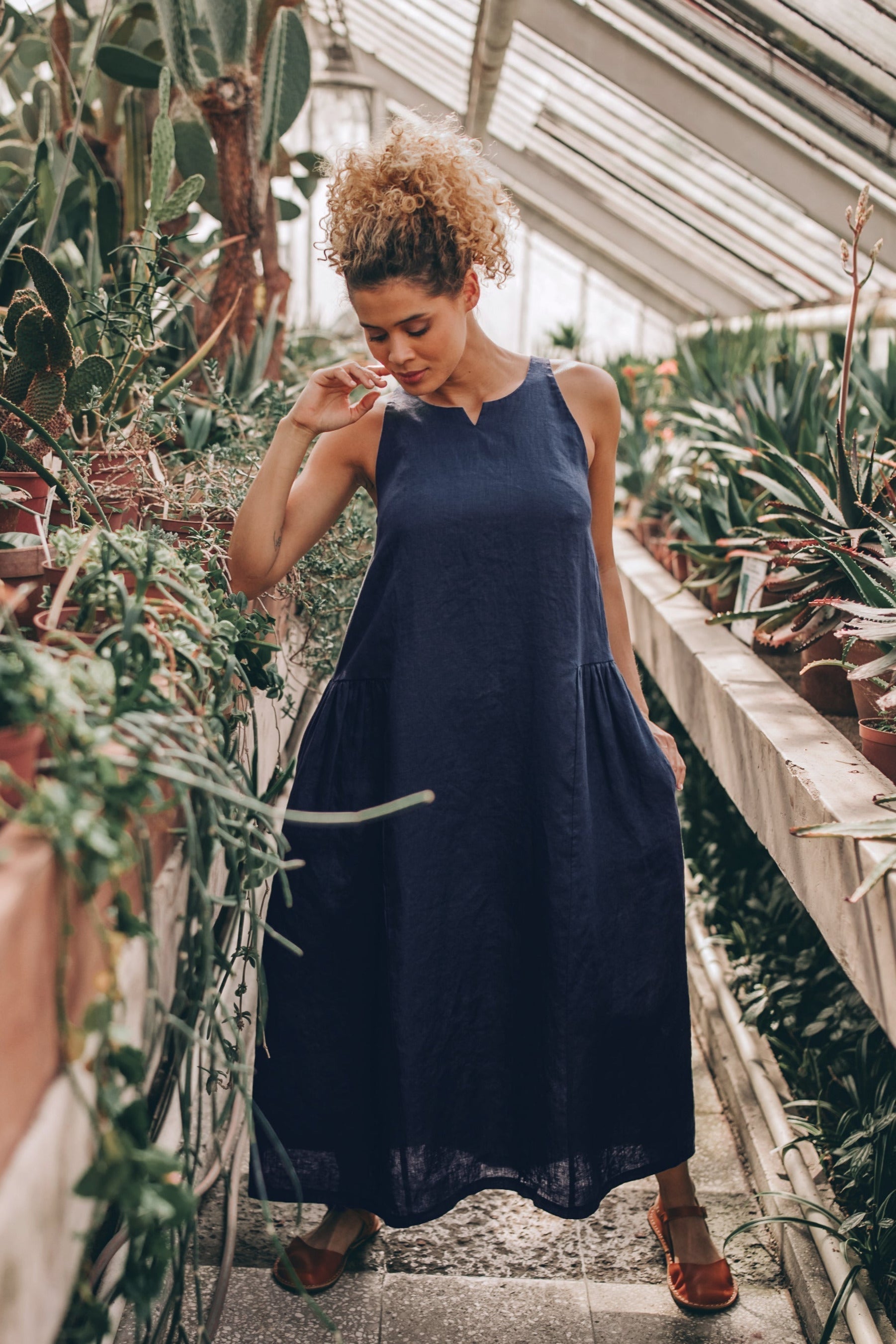 Woman wearing navy loose linen midi dress with pockets in greenhouse setting