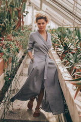 Woman wearing gray linen A-line dress with tie waist in greenhouse setting