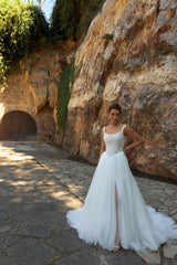 Bride wearing sleeveless A-line wedding gown with boat neckline, pearl and sequin lace bodice, glitter tulle slit skirt, open scoop back, and zip closure.