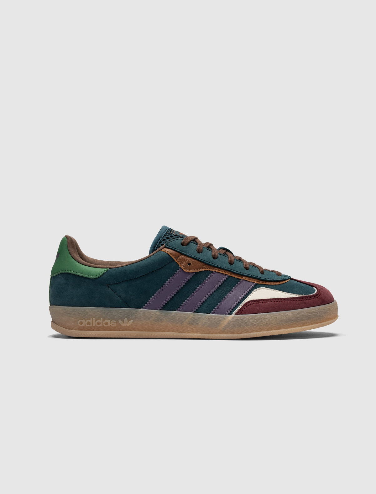 The GAZELLE INDOOR is a low-top Adidas suede sneaker with a gum sole, dark teal upper, green heel, burgundy accents, navy blue tongue, purple Adidas stripes, brown laces, and "adidas" branding on the side.