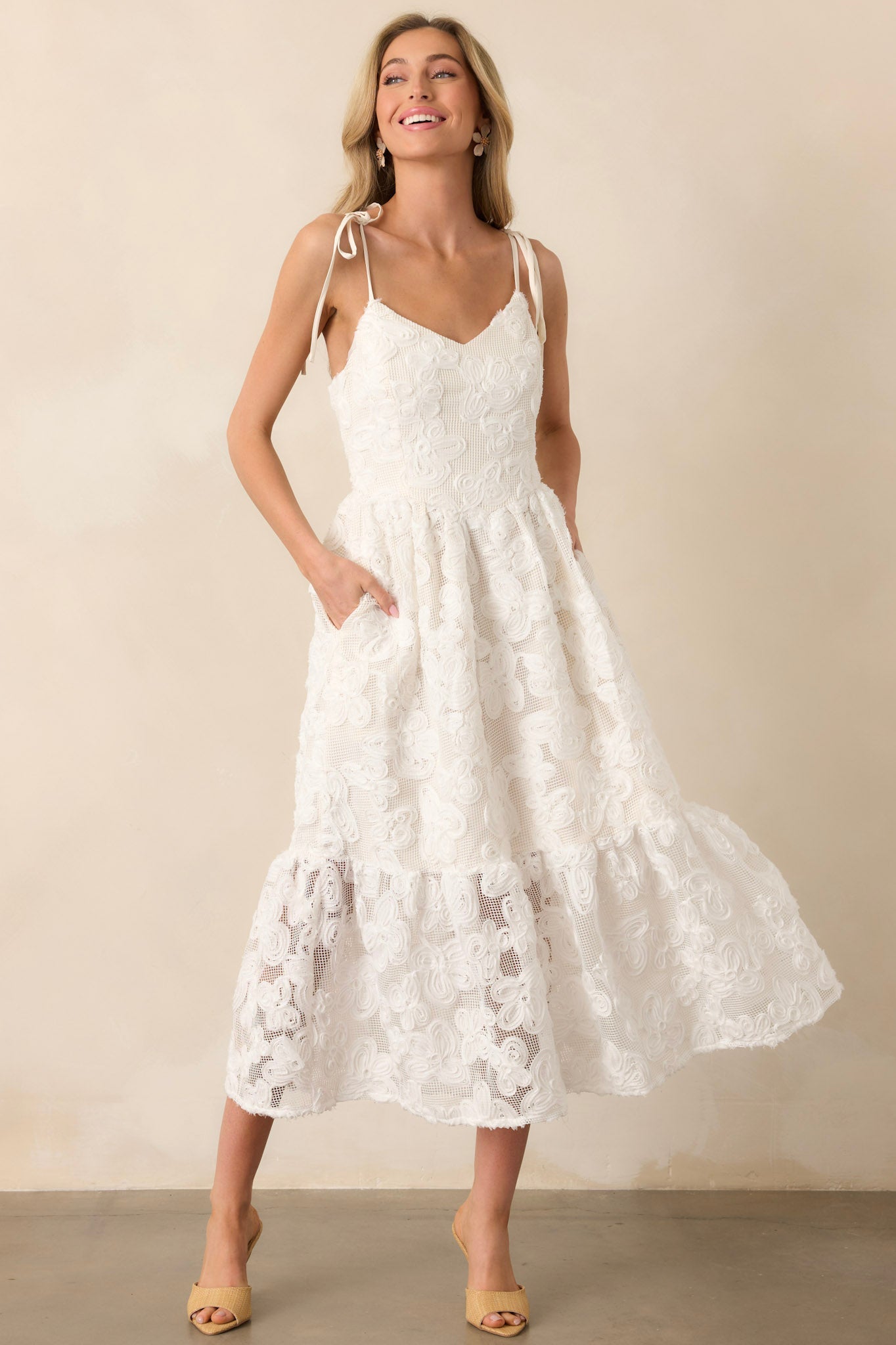 A detailed view of a lace maxi dress with adjustable self-tie bow straps and a hidden back zipper. The floral lace overlay extends past the lining for a sheer, elegant effect.