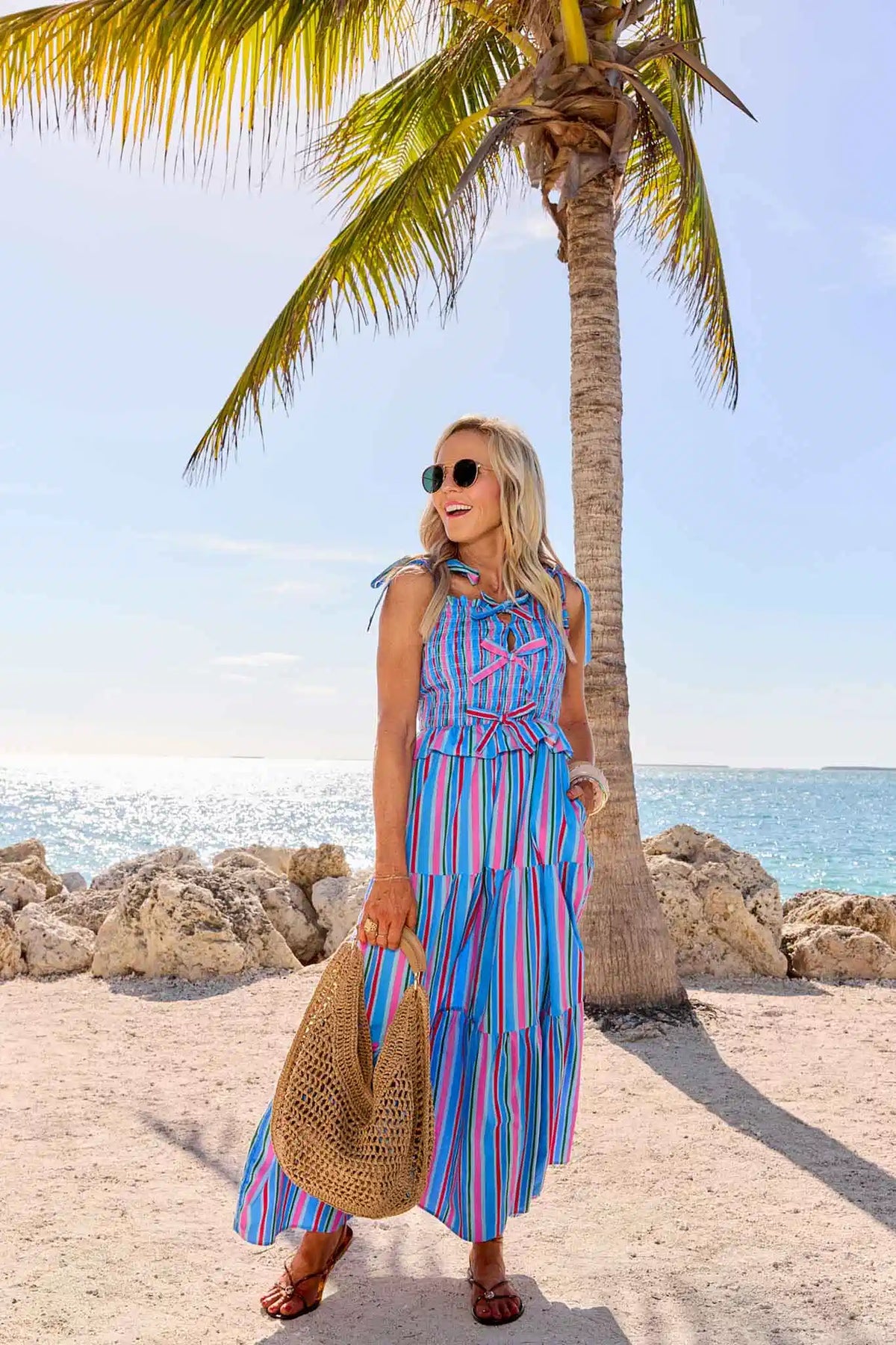 Woman in a blue striped dress standing on a beach with palm trees and ocean in the background