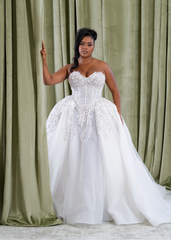 Plus size Black bride wearing a strapless ballgown wedding dress with a sheer corset bodice, exposed boning, crystal appliqué, and full organza skirt, designed by Black bridal brand Pantora.