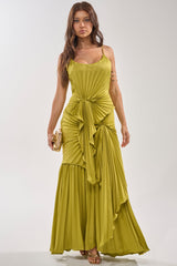 A woman models the RESERVATIONS PLEASE PLEATED MAXI DRESS IN CHARTREUSE, featuring gathered details, while holding a gold clutch and wearing strappy heels—a stunning option for any special occasion.