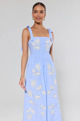 Woman wearing a light blue dress with floral embroidery on a plain background