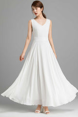 A woman modeling a white chiffon maxi dress with a V neckline and back zip closure, standing on a plain background.