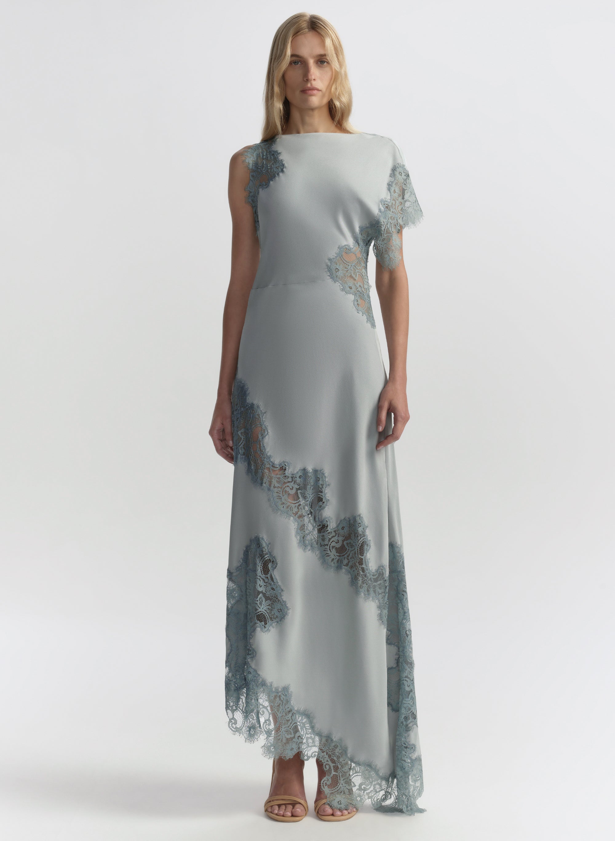 Woman wearing a long, light blue dress with floral lace details on a white background
