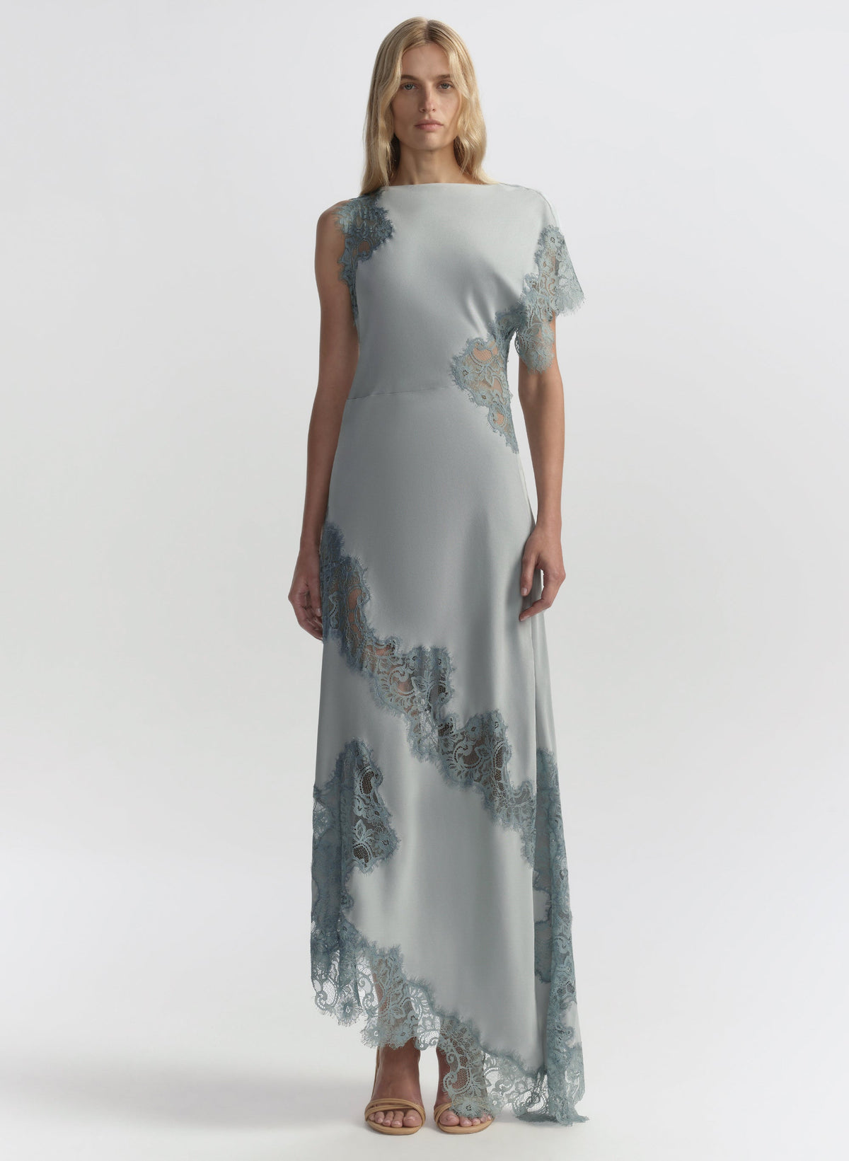 Woman wearing a long, light blue dress with floral lace details on a white background