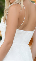 A person with long blonde hair is shown from the back wearing the Velvi Tea-Length White Graduation Dress Sisi, featuring thin straps and eyelet details.