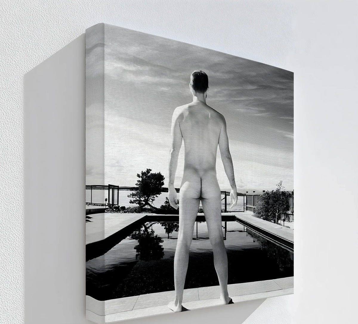 Negative space surrounds a black and white canvas wall art print depicting a nude male figure at a modern pool, emphasizing the stillness.