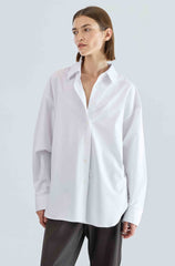 Woman wearing a white shirt and dark pants on a light gray background