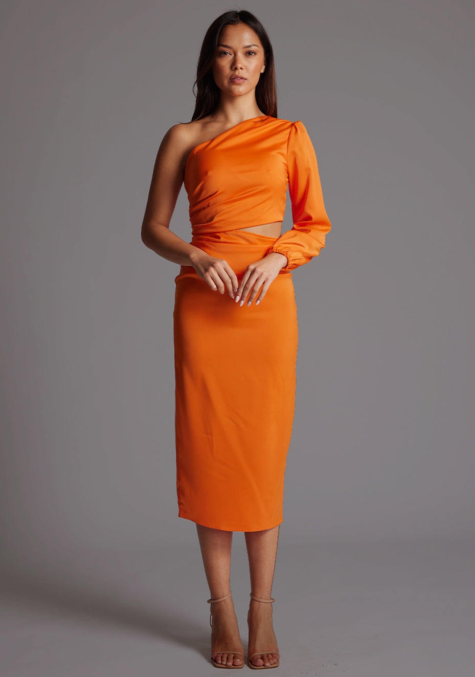 Front image of a model wearing an orange mid dress with a asymmetric, one long sleeve design and subtle side cut-out.  The design featured is the Vesper Niccola Orange Midi Dress