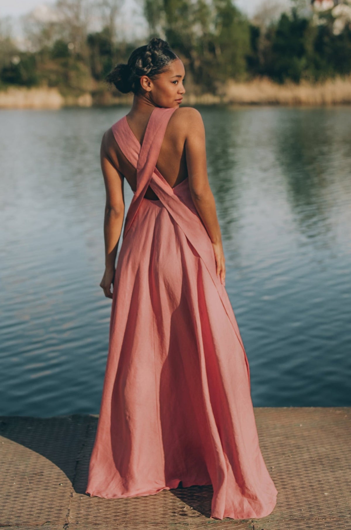 Woman wearing a pink cross-back linen dress standing by the water
