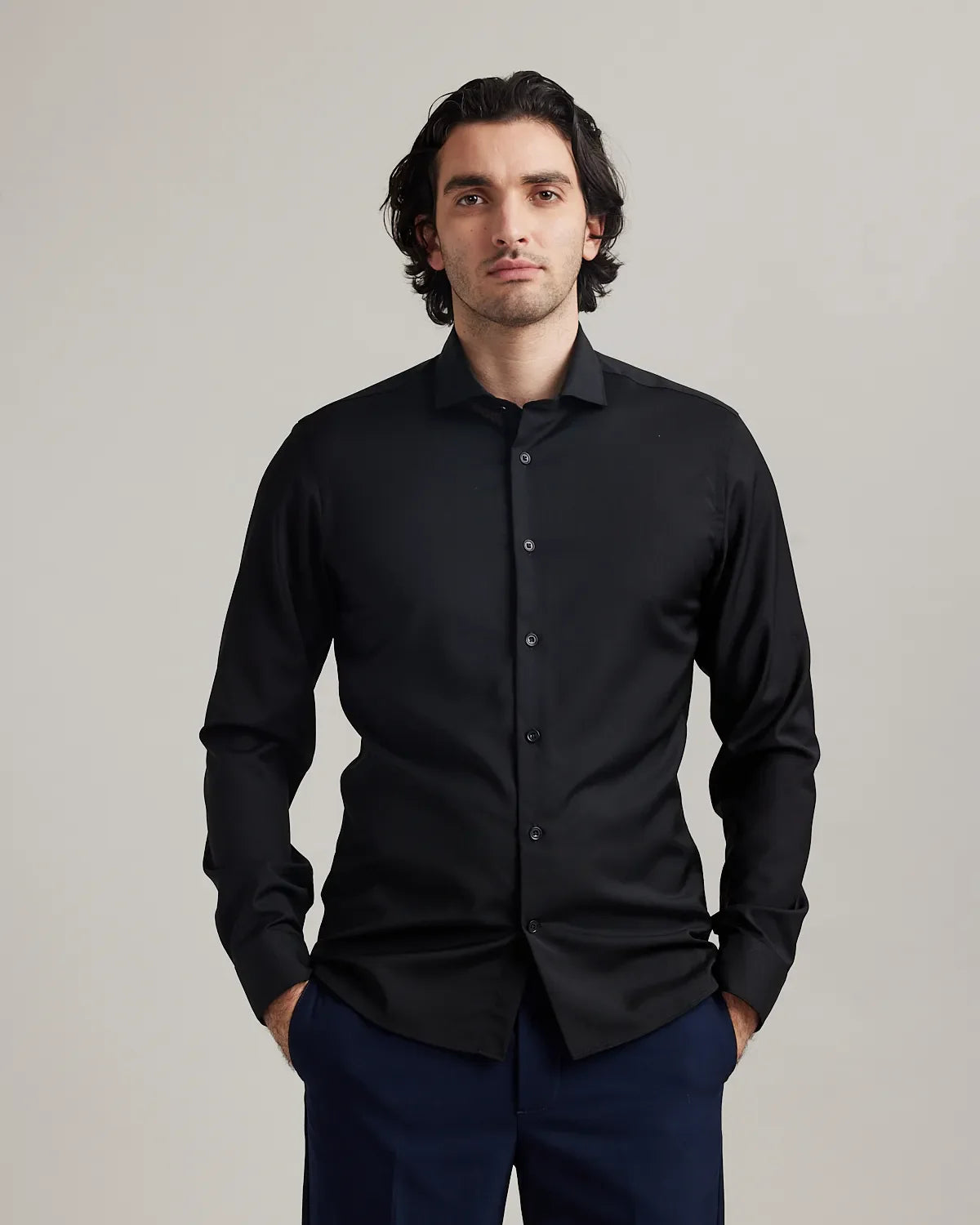 Man wearing a black merino dress shirt from Wolk and navy pants against a plain background