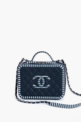 A small rectangular quilted navy vanity bag from the Tuckernuck Archive Collection, featuring a top handle, chain strap, striped edges, and a silver logo on the front.