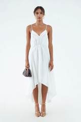White silk-hemp dress with thin shoulder straps, V neckline, waist gather, and flared, asymmetrical hem that waterfalls around the legs. Worn with gold sandals and maroon clutch.