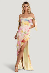 Front view of yellow multi-floral off-shoulder chiffon maxi dress showing cowl neckline, adjustable bow straps, and tulip skirt in motion.