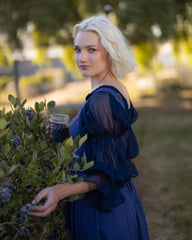 Woman in navy blue chiffon chemise picking blueberries outdoors in soft natural light with puff sleeves and flowing fabric