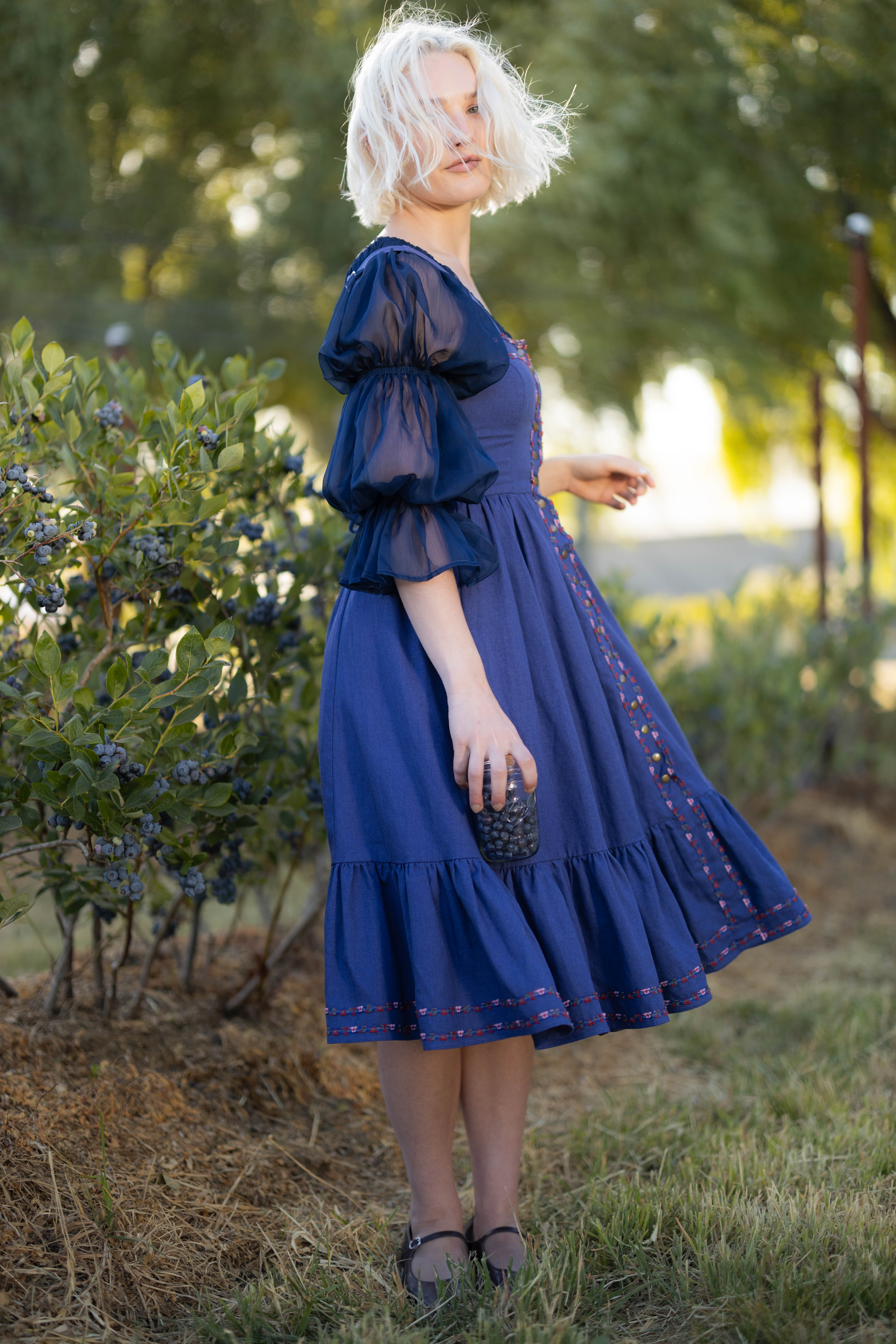 Woman wearing navy blue chiffon chemise with puff sleeves holding a cup of blueberries outdoors in natural light