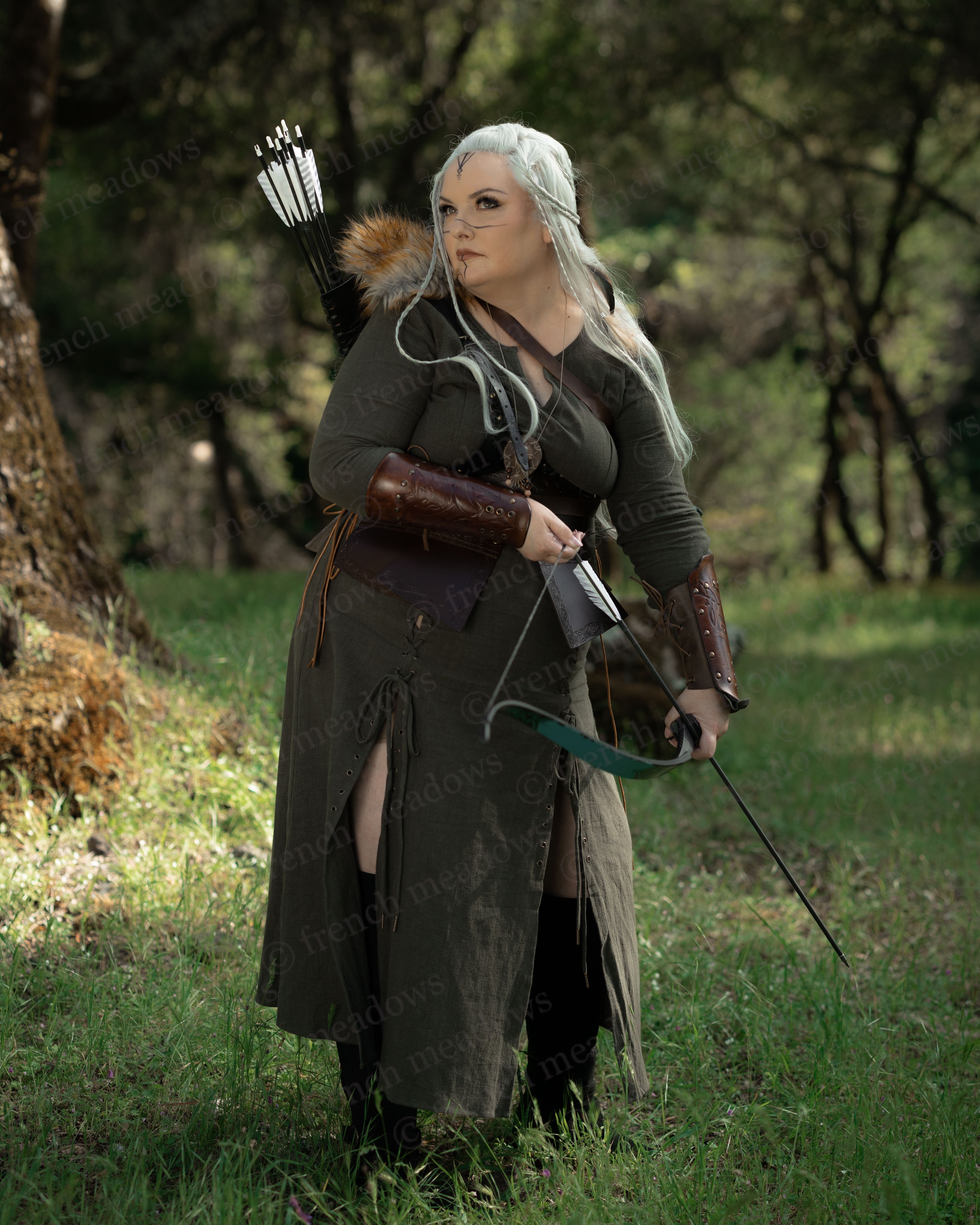 Woman in forest wearing Olive Green Viking Dress with bow and arrow dressed for Renaissance or Viking cosplay