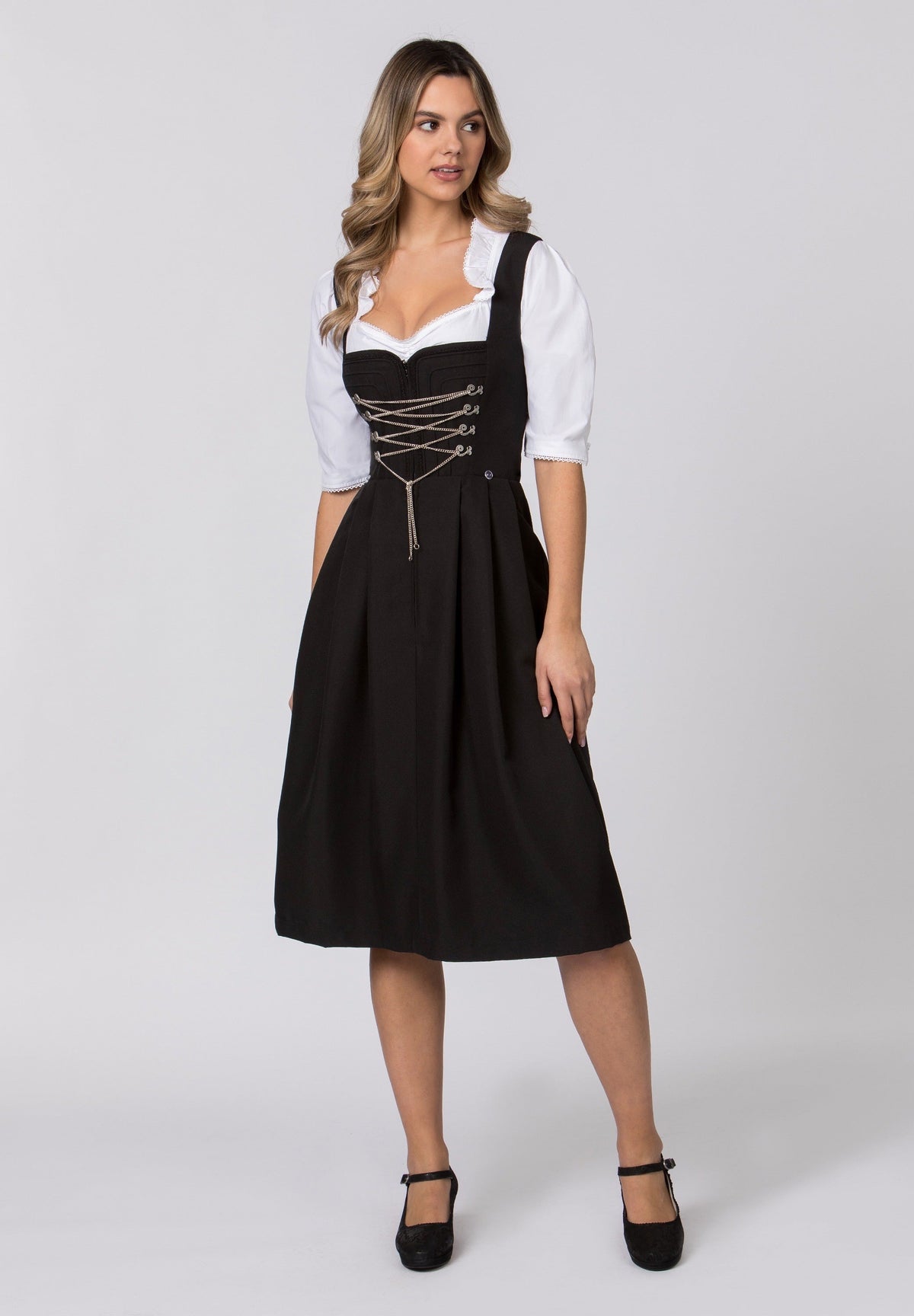 A woman wearing a black Adele long dirndl dress with a white blouse  standing against a plain background.