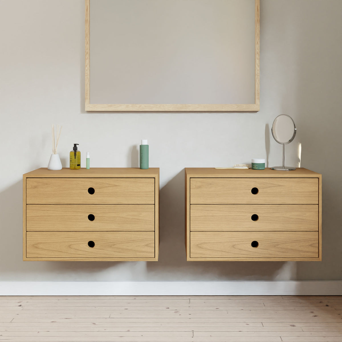Two Krovel Hardwood Floating Dressers are mounted on a light wall below a large wooden-framed mirror; the left dresser stores toiletries, while the right holds a small round mirror and other items. The floor is light wood.#wood_cherry