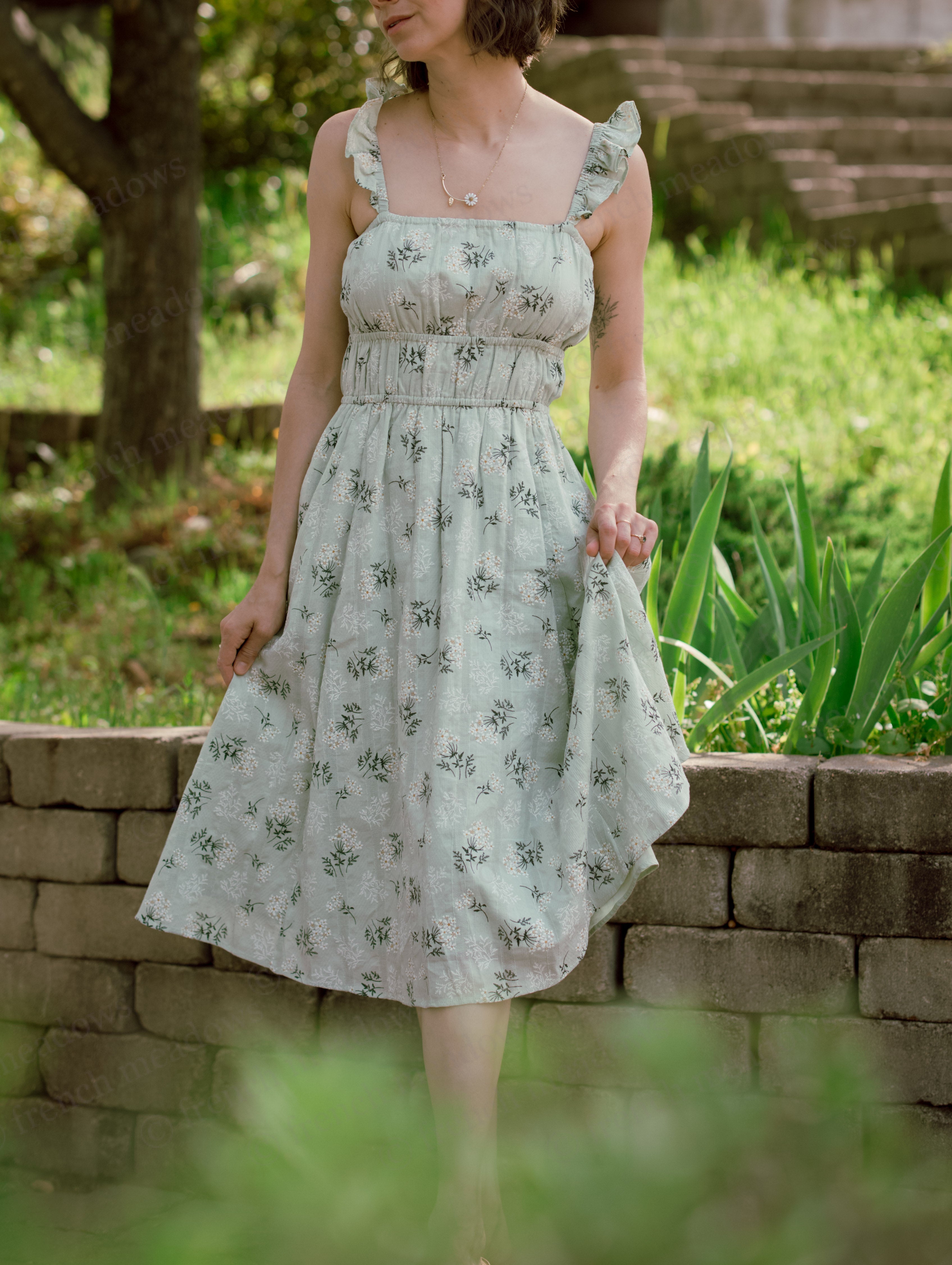 Woman wearing a Floral Milkmaid Dress with ruched bodice and A-line skirt standing outdoors by stone wall.