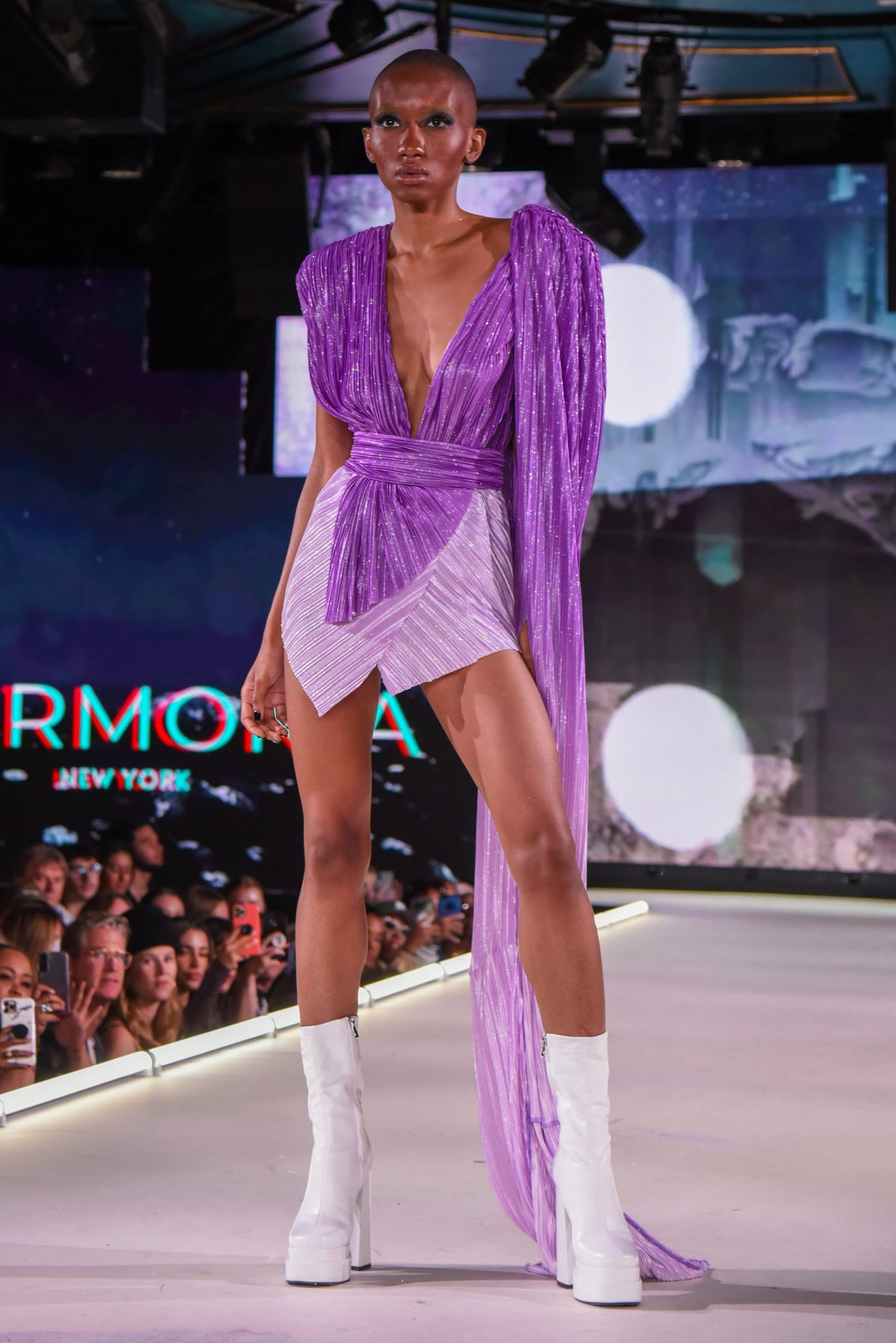 Model struts in shimmering purple HARMONIA NY stage wear with white platform boots on runway