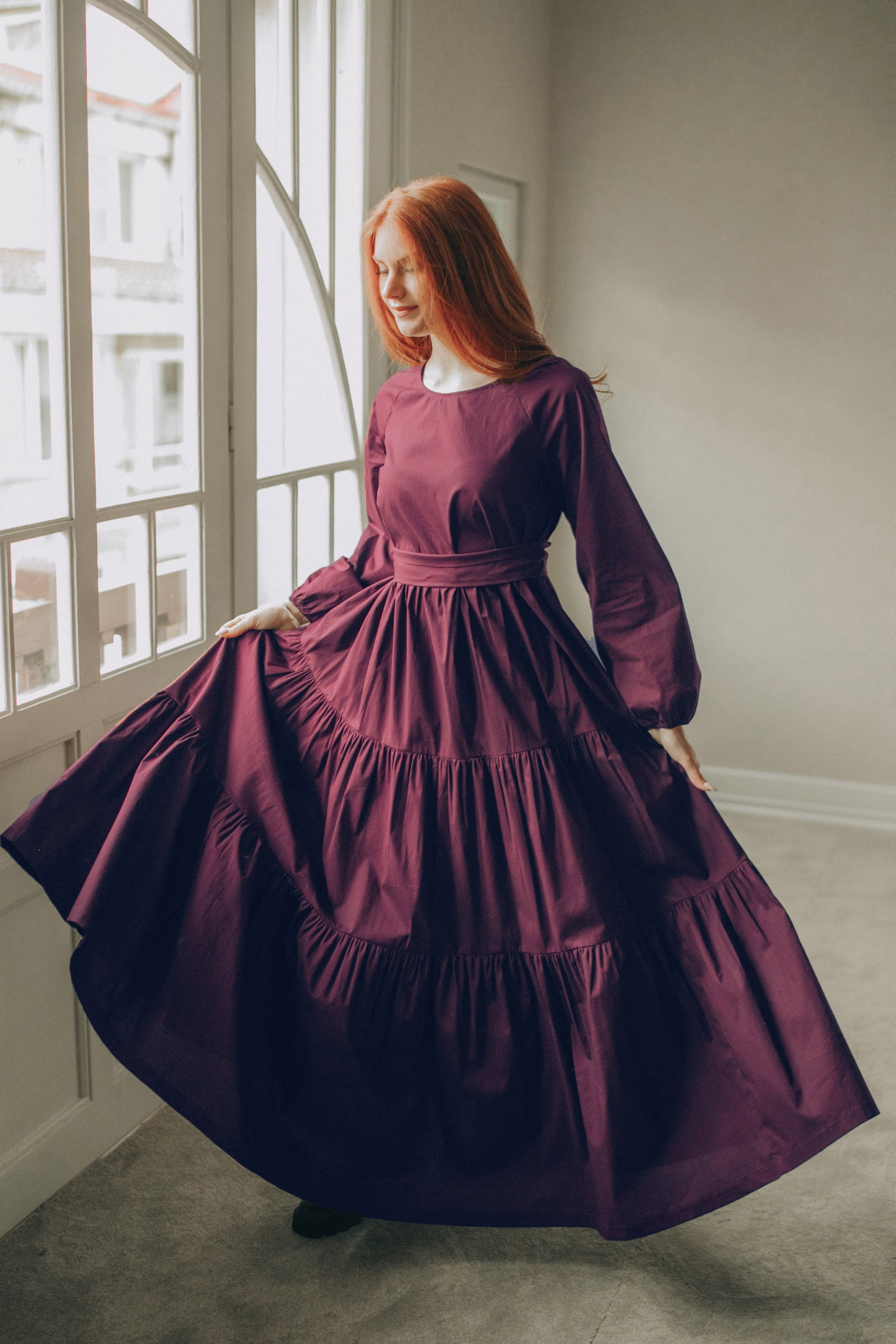 Woman wearing deep burgundy tiered cotton maxi dress with adjustable tie waist and flowing skirt