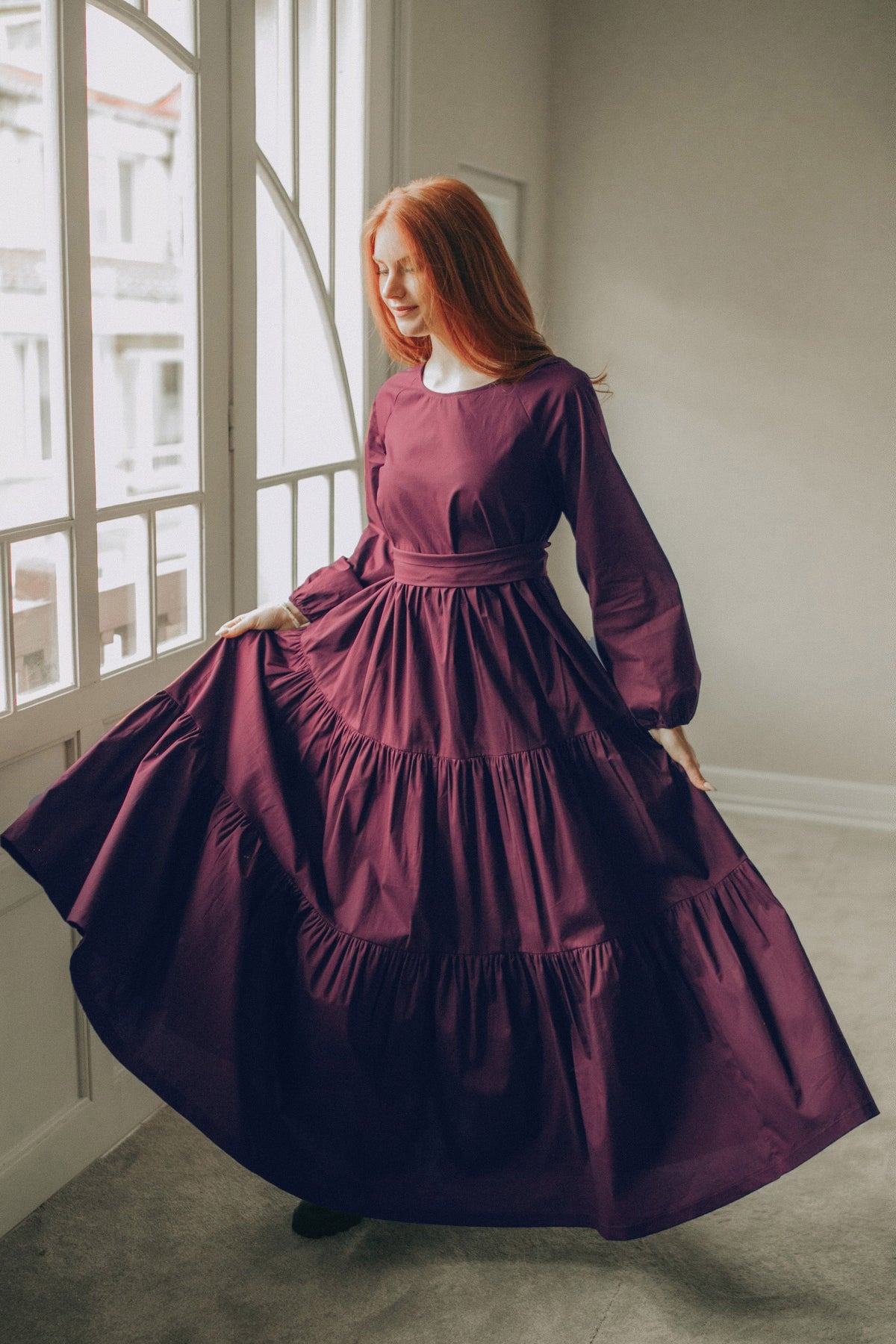 Woman wearing deep burgundy tiered cotton maxi dress with adjustable tie waist and flowing skirt