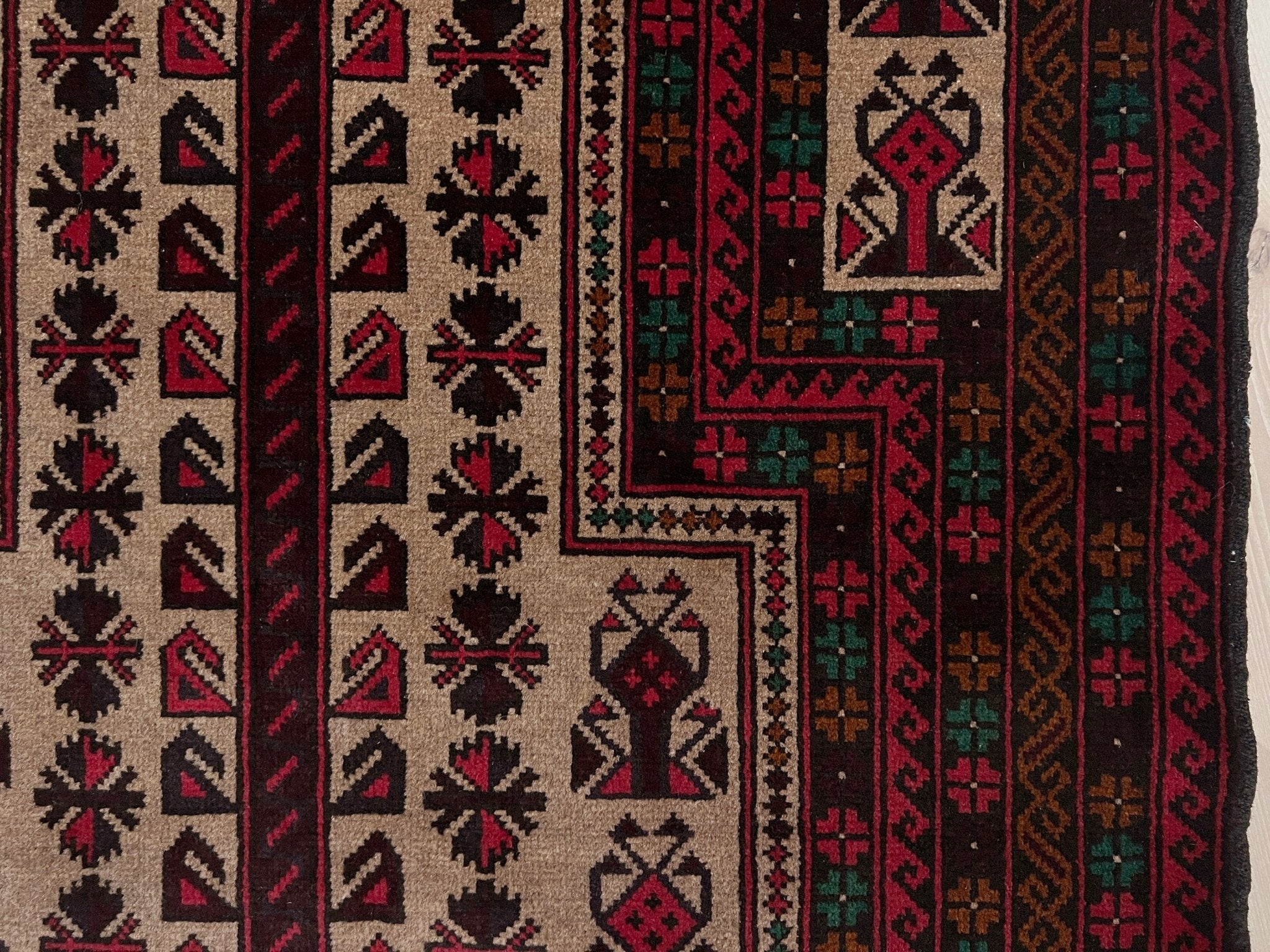 Side detail of a Baluch Turkmen Prayer Rug - Handmade Wool Carpet in a 3x5 size, featuring traditional tribal geometric patterns with rich red, black, beige, green, and teal colors. Ideal for living room, bedroom, kitchen, entryway, or nursery decor. Available at a handmade rug shop in the San Francisco Bay Area.