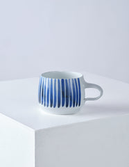 Front view of white porcelain cup with hand painted blue vertical stripes.