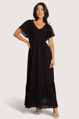 Front view of Monica Smocked Maxi Dress in black chiffon showing V-neckline, center-seamed smocked bodice, flutter sleeves, and flowing maxi skirt.