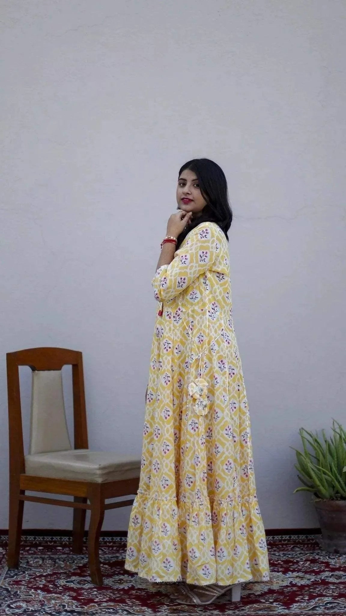 Woman wearing yellow mulmul cotton gown with floral print, standing on patterned carpet indoors