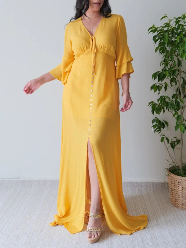 Front view of a woman wearing a mustard yellow maxi dress with sleeves and a front slit, showing decorative buttons.