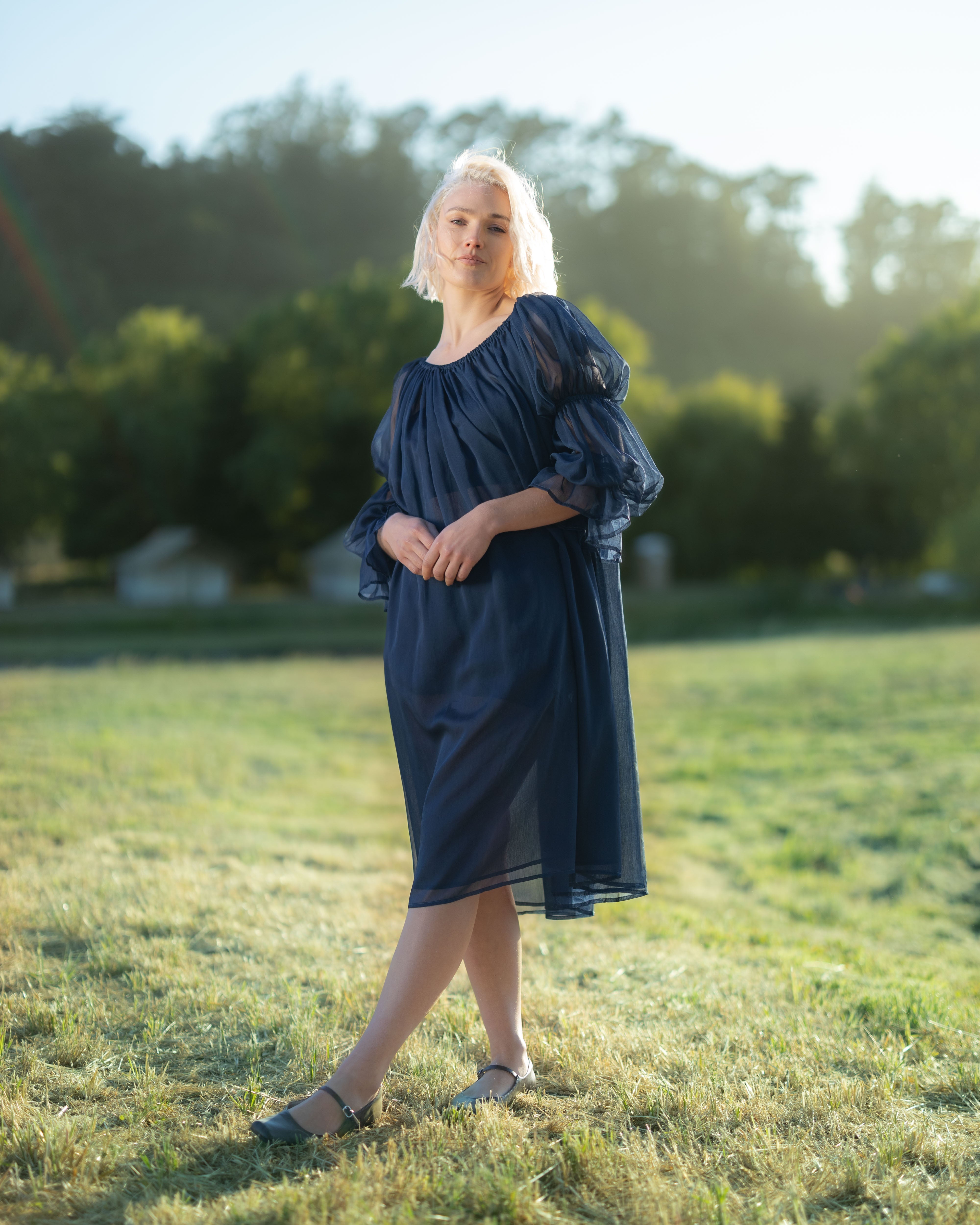 Woman wearing a navy blue chiffon chemise with puff sleeves standing outdoors in soft sunlight