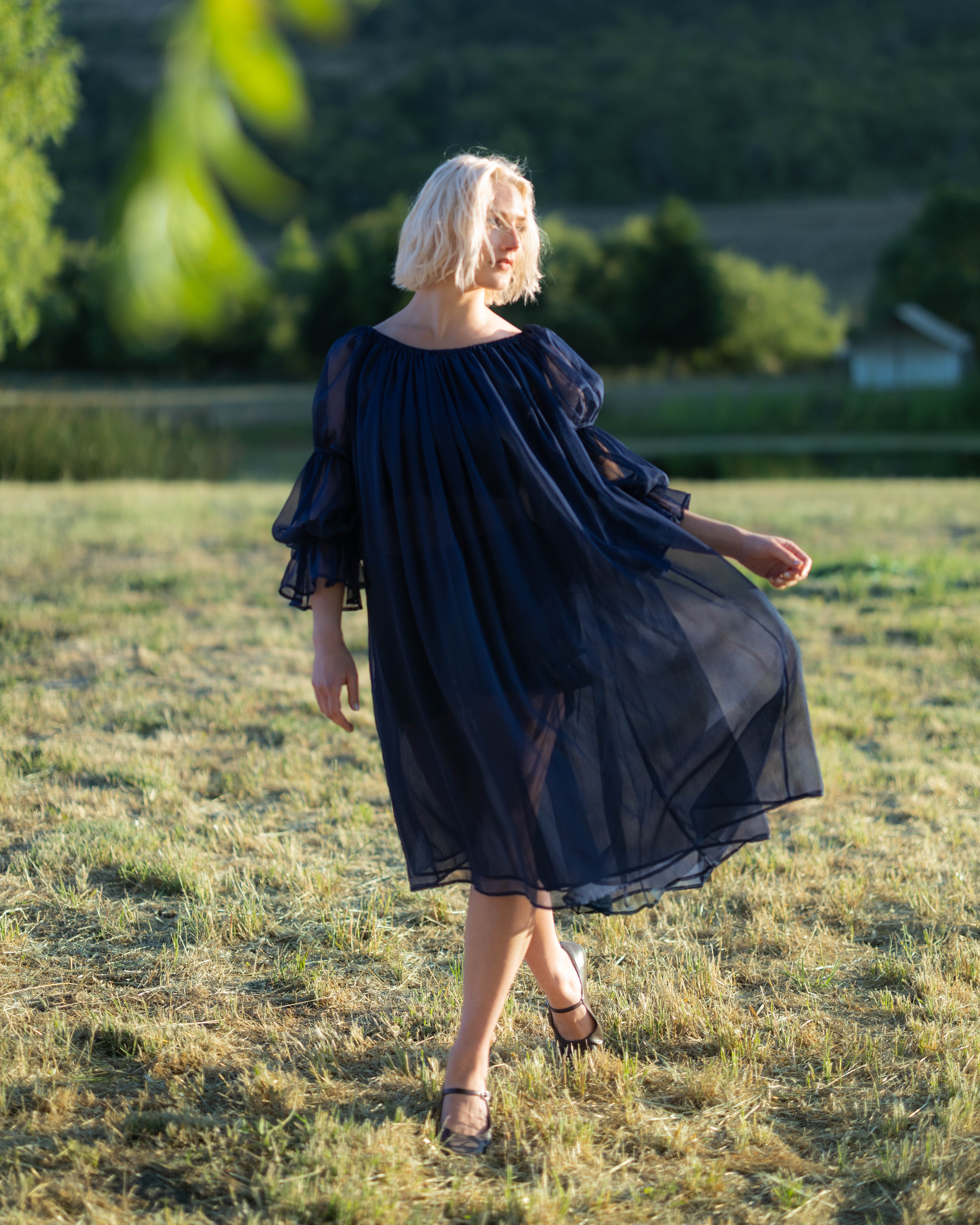Woman outdoors wearing a flowing navy blue chiffon chemise with puff sleeves and elastic cuffs in natural light