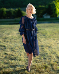 Woman wearing a navy blue chiffon chemise with puff sleeves and a black belt standing outdoors in a grassy field