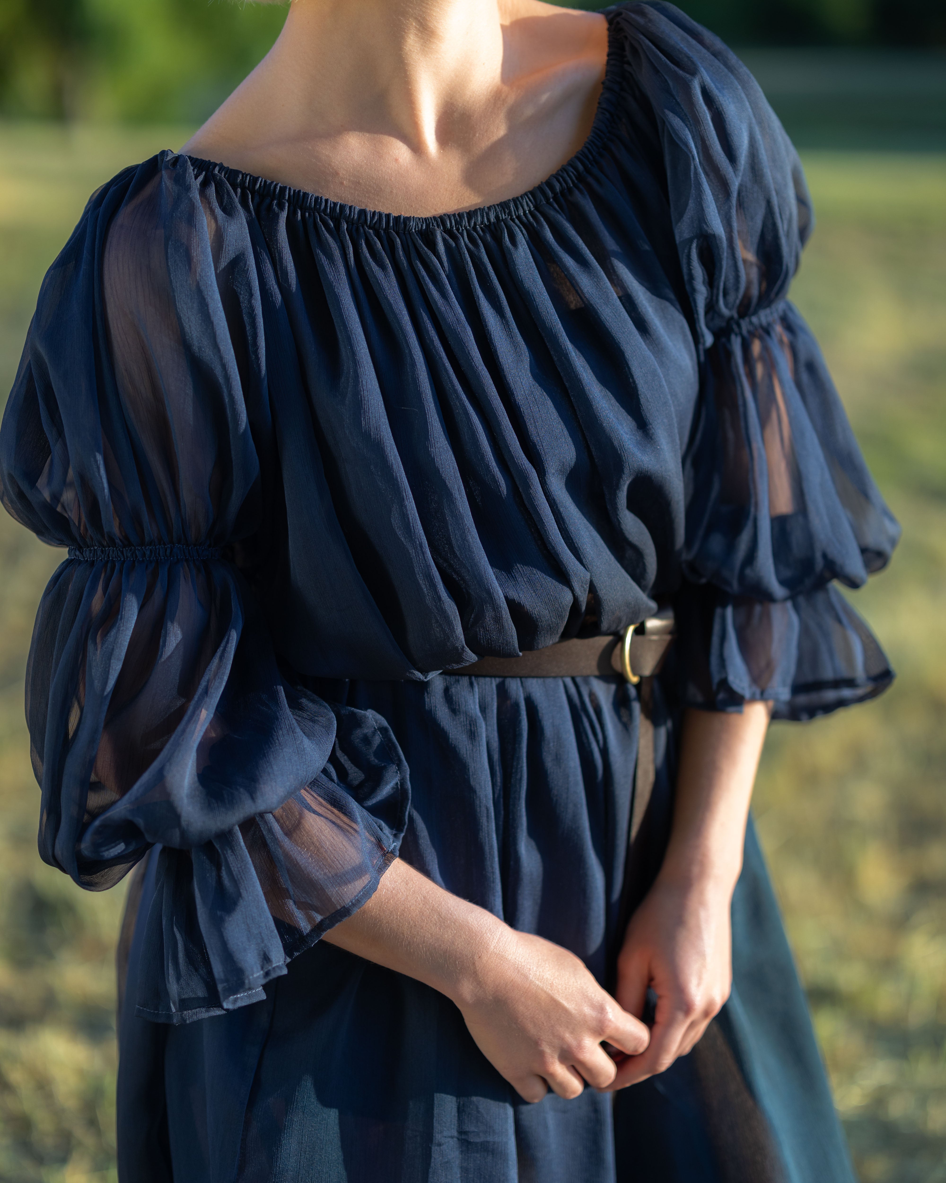 Woman wearing navy blue chiffon chemise with puff sleeves and elastic cuffs outdoors in natural light