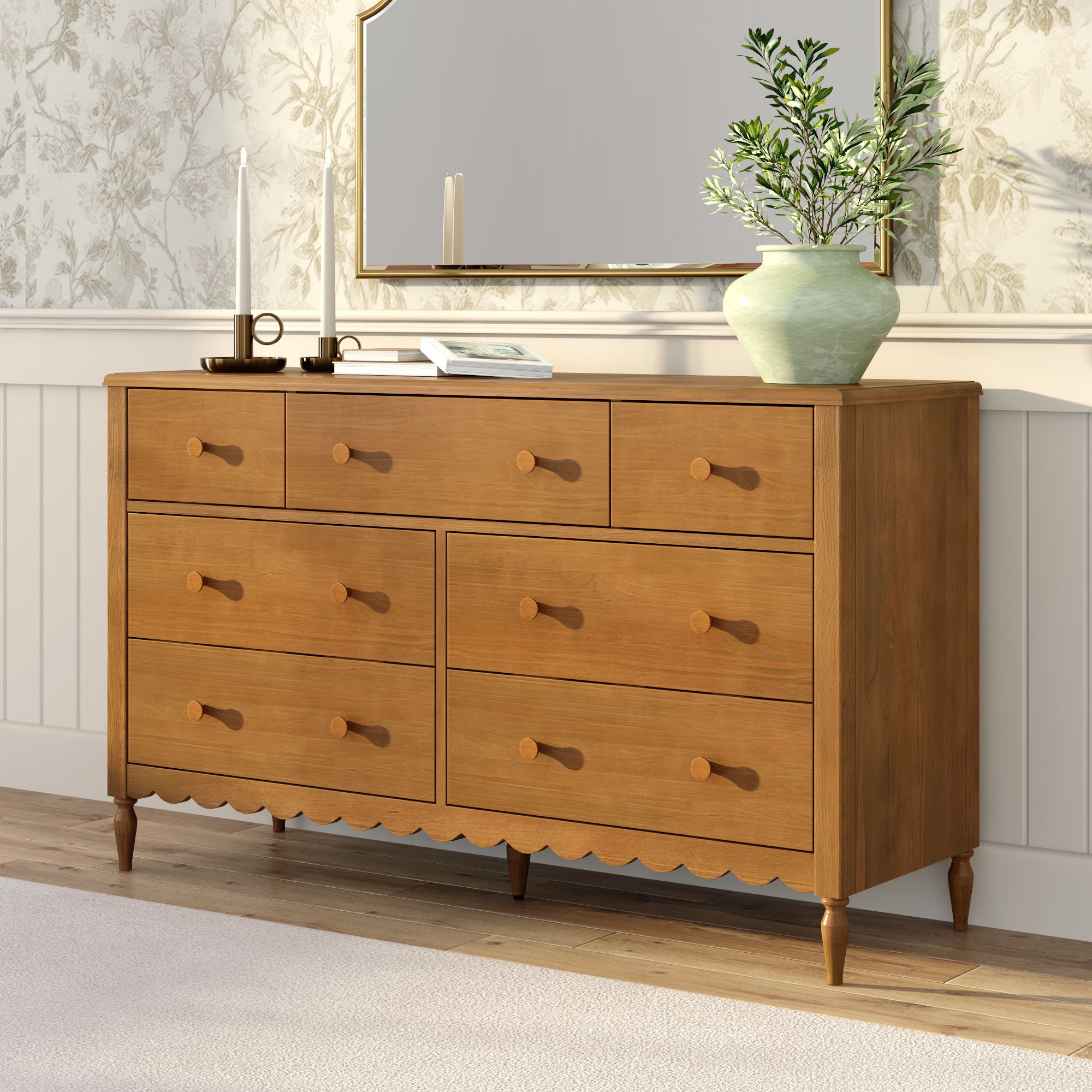 Light oak solid wood dresser with multiple drawers and scalloped apron, styled with green ceramic vase, books and candles under a gold-framed mirror in a bright farmhouse bedroom — ideal bedroom storage and home decor