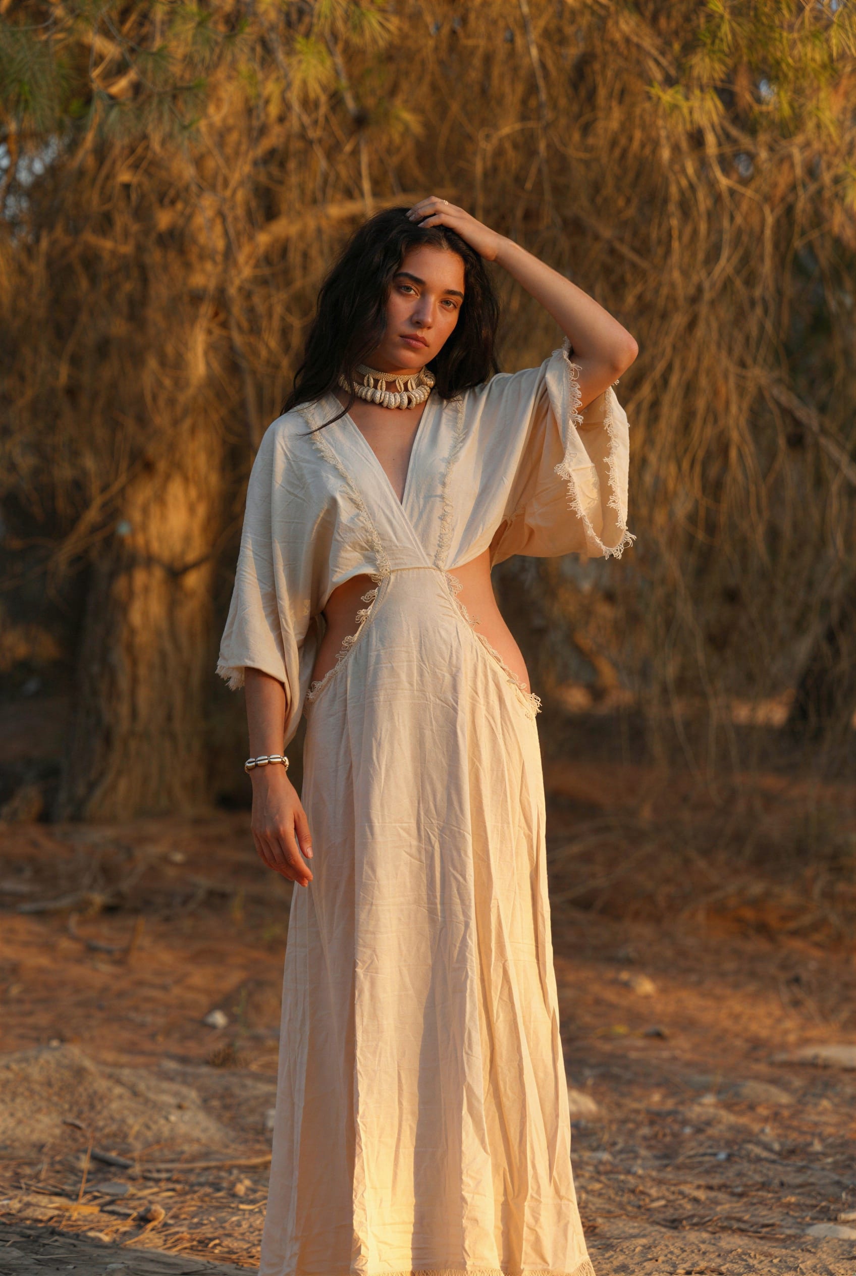 Woman in a white raw silk dress with a priestess, fairy dress feel, standing in warm sunlight.