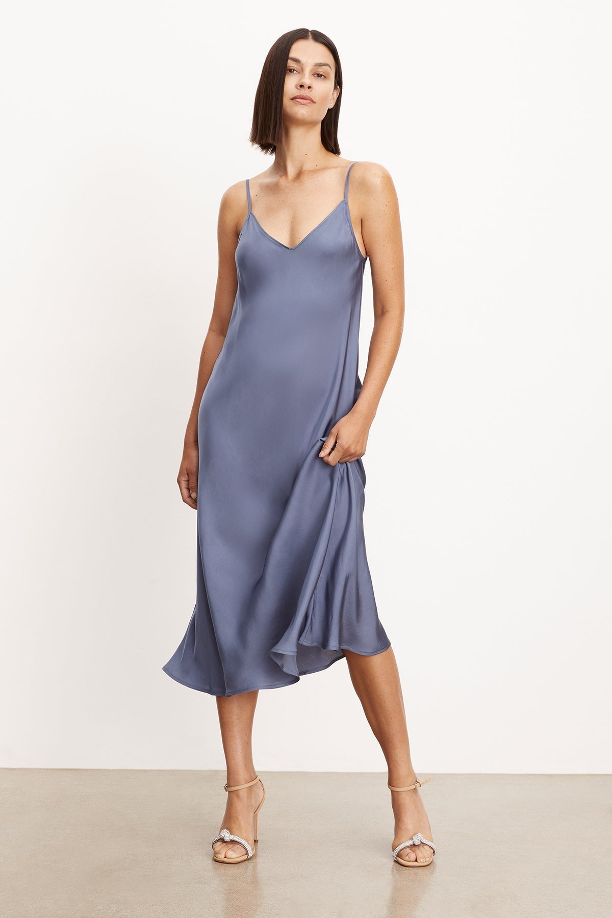 The model is wearing a blue Velvet by Graham & Spencer POPPY SATIN SLIP DRESS with adjustable straps, showcasing its versatility.