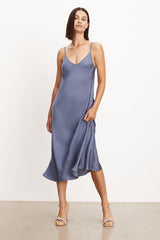 The model is wearing a blue Velvet by Graham & Spencer POPPY SATIN SLIP DRESS with adjustable straps, showcasing its versatility.
