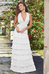 A woman in a tiered white dress stands in an outdoor setting, smiling and posing. The background features greenery and a stone path framed by flowers, suggesting a picturesque garden.