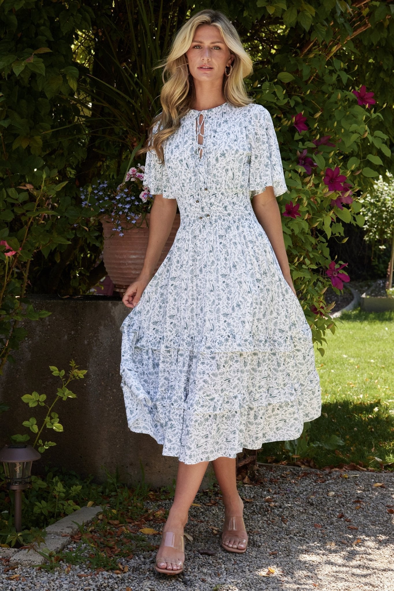 Front model view of white and sage floral boho midi dress with V-neck, smocked waist, and mid-thigh lining, shown on model.
