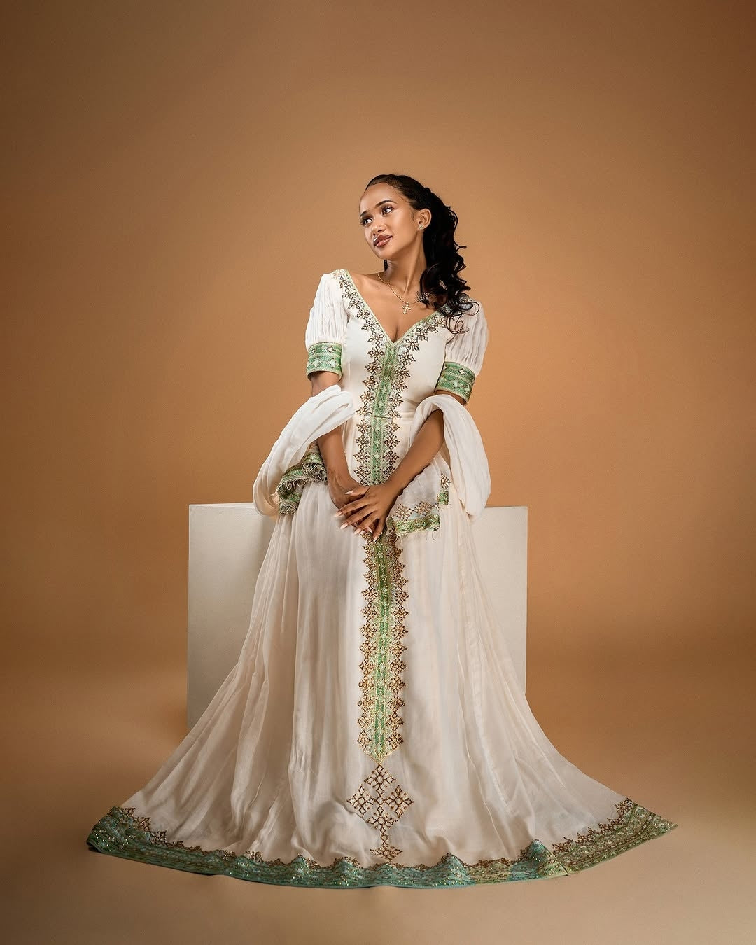 Woman wearing a white dress with green embroidery on a beige background